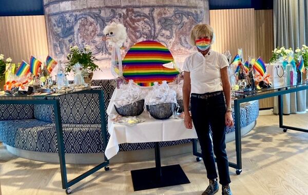 Co-Organisatorin Brigitte Felske vor den reich gedeckten Gabentischen voller Preise und Tee-Geschenke. Überall leuchten die Regenbogenfarben